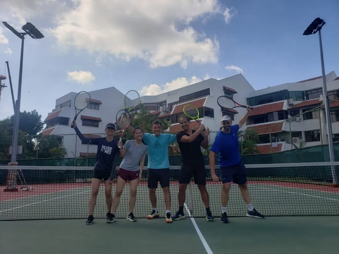 A small group of adults having fun after a tennis session at a Singapore condo court