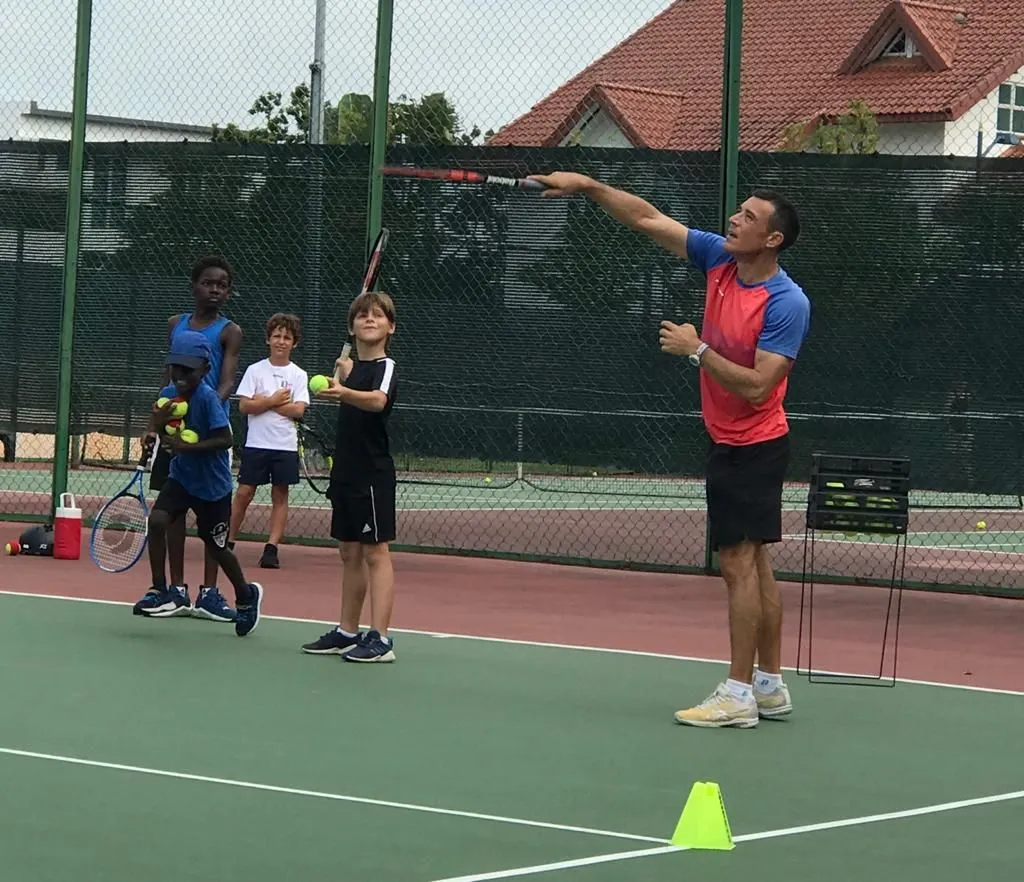 A Pure Sport coach demonstrating a serve to a junior group during a structured academy session