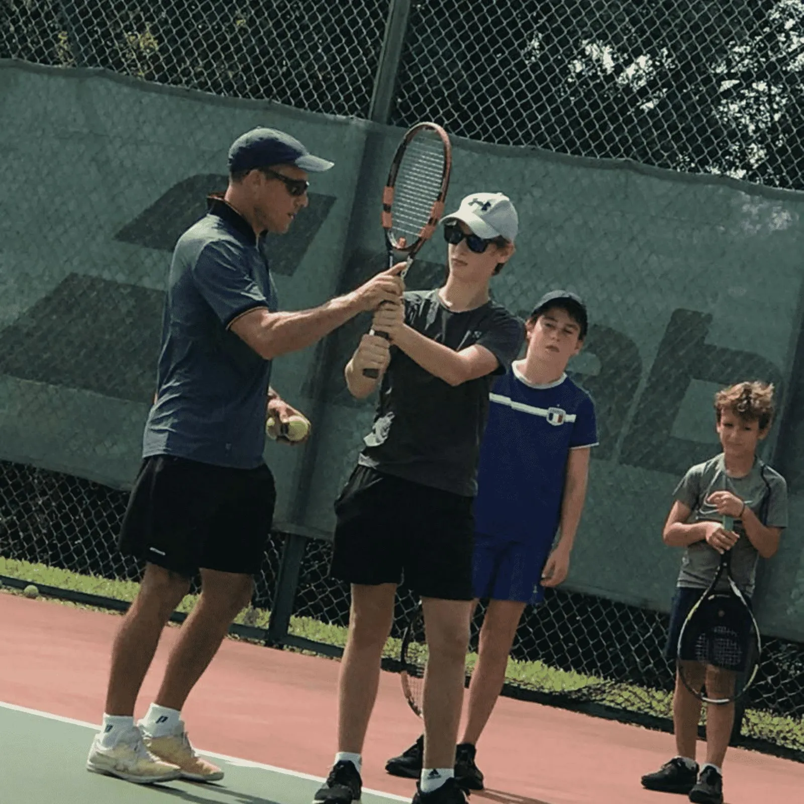 A coach correcting a teenage player's grip during a tennis session